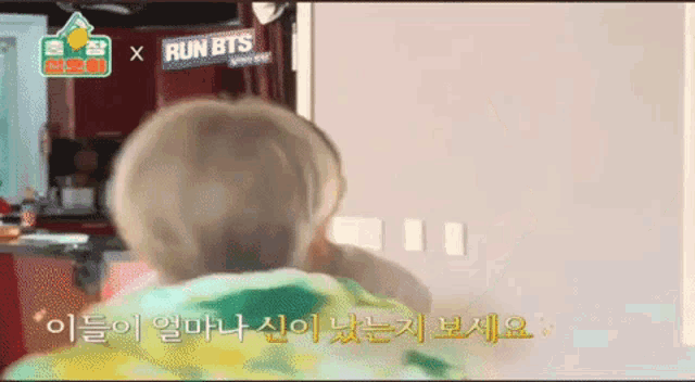 a baby is sitting in front of a wall with a sign that says run bts