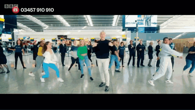 a group of people are dancing in an airport and the number 03457 910 910 is on the bottom of the screen