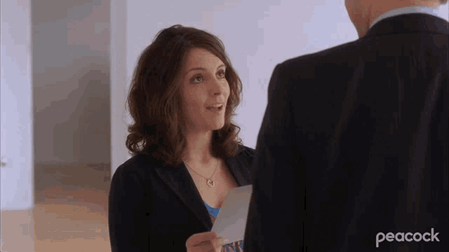 a woman in a suit is holding a piece of paper in front of a man in a suit with peacock written in the corner