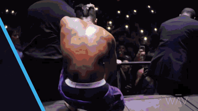 a man in purple shorts is squatting down in front of a crowd with a security guard behind him