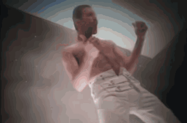 a shirtless man in white pants is dancing on a stage in a dark room .