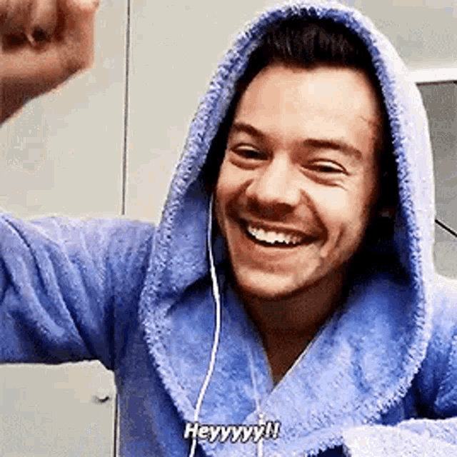 harry styles is wearing a blue robe and headphones and smiling while taking a selfie .