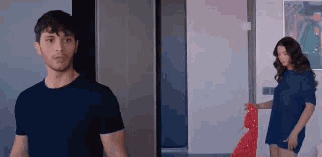 a man and a woman are standing next to each other in a room . the man is wearing a blue shirt .
