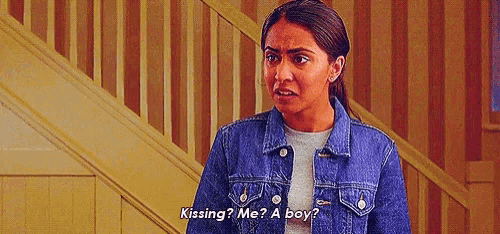 a woman in a denim jacket is standing in front of a staircase and talking to a boy .
