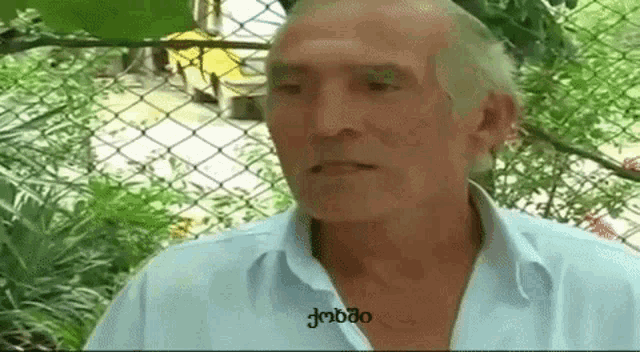 a man in a blue shirt is standing in front of a chain link fence and talking to someone .