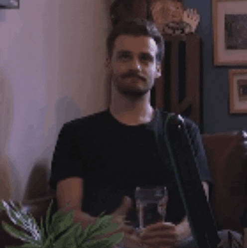 a man is sitting on a couch holding a glass of water in his hand .