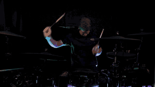 a man is playing drums in a dark room with a shirt that says ' acdc ' on it