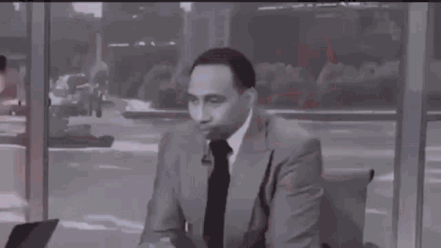 a man in a suit and tie is sitting in a chair in front of a mirror .