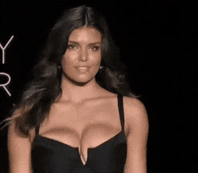 a woman is walking down a runway wearing a black bra and earrings .