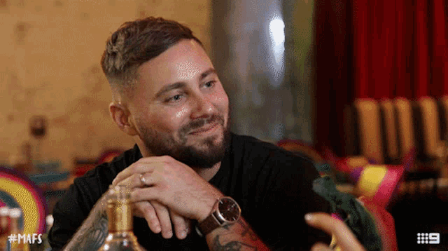 a man with a beard is sitting at a table with a bottle of whiskey and the number 9 on the bottom left