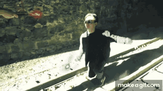a person is standing on a sidewalk with their arms outstretched in front of a stone wall