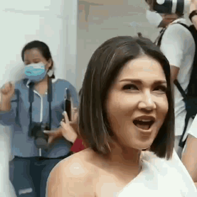 a woman is wearing a mask and making a funny face while standing in front of a group of people .