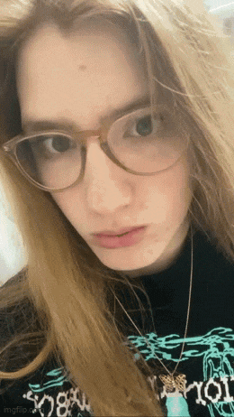 a girl wearing glasses and a necklace is looking at the camera .
