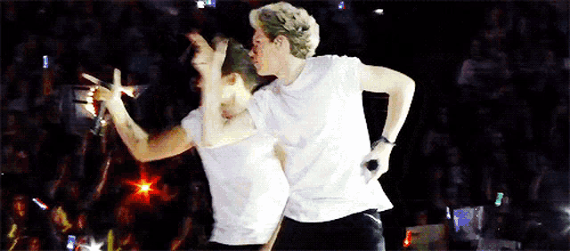 two men in white shirts are dancing on a stage with a crowd behind them .