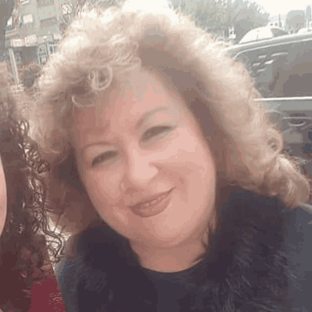 a woman with curly hair is smiling for the camera while wearing a black fur collar .