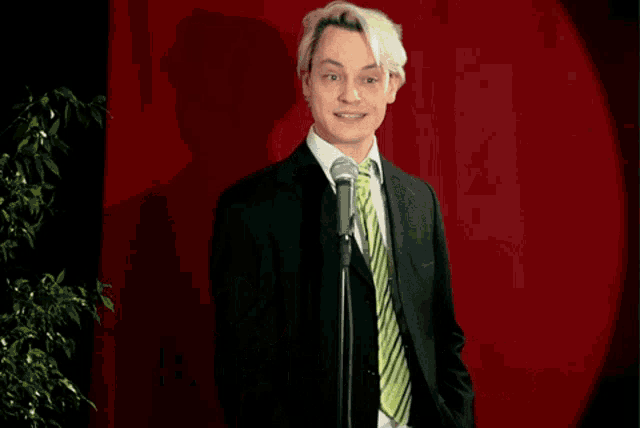 a man in a suit and tie stands in front of a microphone with the words " a bit desperate " below him