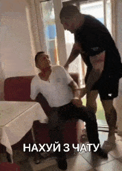 a man is standing next to another man who is sitting on a couch in a living room .