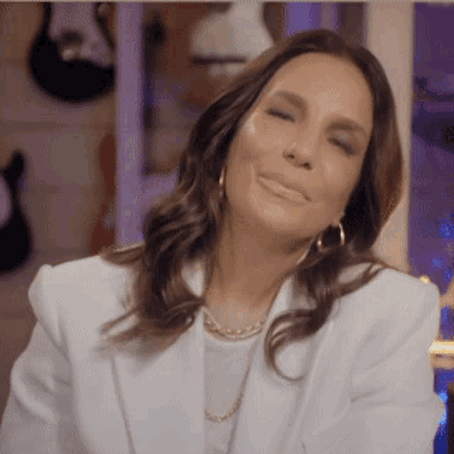a woman wearing a white jacket and hoop earrings is smiling .