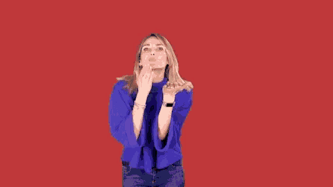 a woman in a blue sweater is pointing at the camera with her hands .
