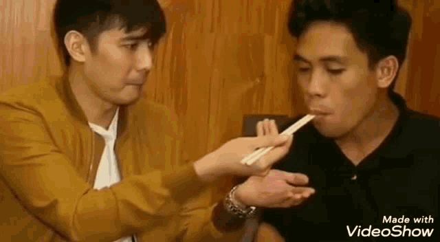 a man is feeding another man with chopsticks at a restaurant .