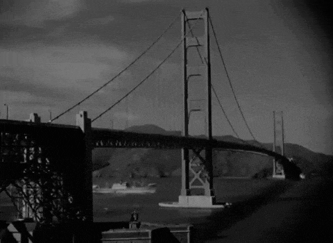 a black and white photo of a bridge over a body of water with mountains in the background
