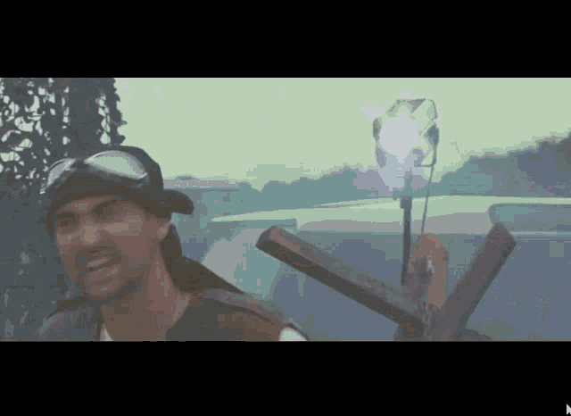 a man wearing goggles and a hat is holding a cross in front of a car