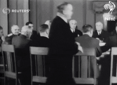 a man stands in front of a group of men sitting around a table with reuters written on the bottom
