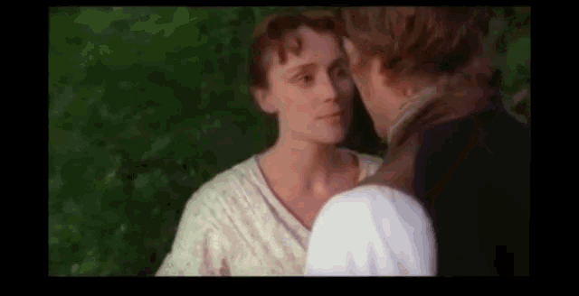 a man and a woman are kissing in front of a green forest .