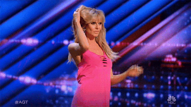 a woman in a pink dress is dancing on a stage with her hands in her hair .