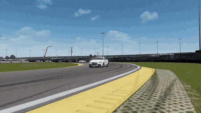 a white car is driving on a race track with a yellow curb