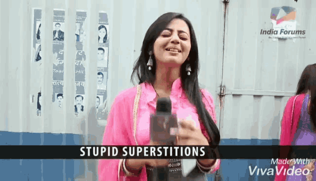 a woman is holding a microphone in front of a wall that says stupid superstitions