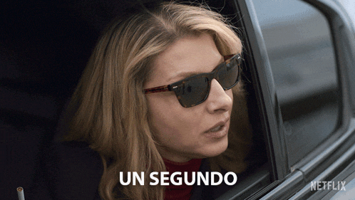 a woman wearing sunglasses is looking out of a car window with the words un segundo written below her