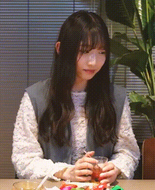 a woman is sitting at a table with a cup of tea in her hand and a plant in the background .