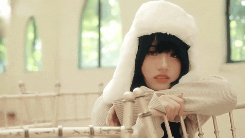 a girl wearing a white sweater and a furry hat leans on a railing