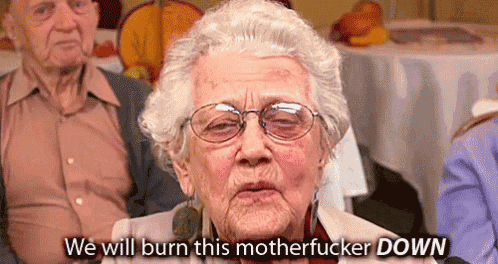 an elderly woman wearing glasses says we will burn this motherfucker down in front of a group of people .