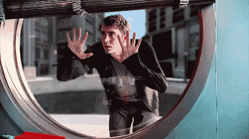 a man looks out of a round window with his hands on the glass