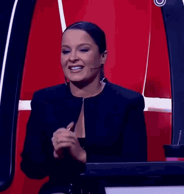 a woman in a black jacket is sitting in front of a red chair and smiling .