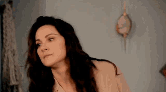 a woman with long hair is standing in front of a blue wall and looking at the camera .