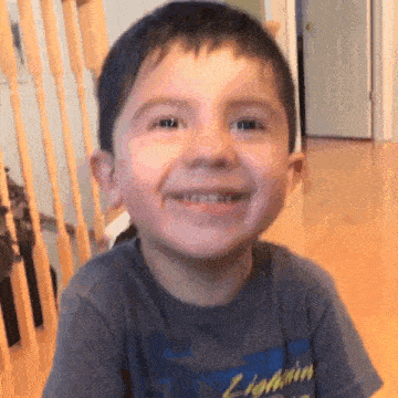 a young boy is smiling and looking at the camera while wearing a lightning bolt shirt .