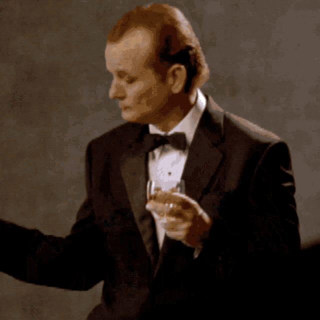 a man in a tuxedo holds a glass of whiskey in front of a sign that says ' galician '