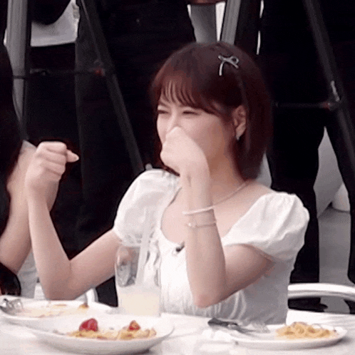 a woman is sitting at a table with plates of food and covering her face with her hand .