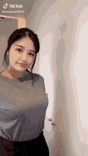 a woman in a grey shirt is standing in front of a white wall .