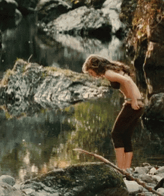 a woman in a bikini is standing on a rock near a body of water