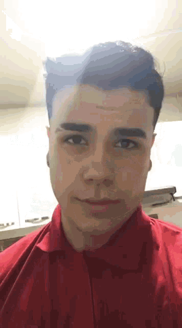a young man is wearing a red shirt and looking at the camera