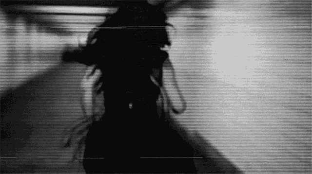 a black and white photo of a woman 's silhouette walking down a hallway .