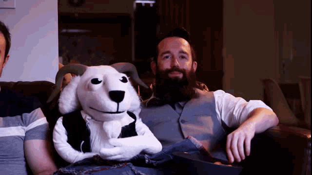 a man with a beard sits on a couch with a stuffed animal