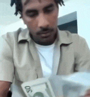 a man in a tan shirt is holding a pile of money .