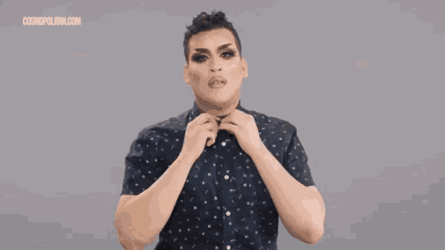 a drag queen wearing a black dress and a black jacket is standing with her arms outstretched .