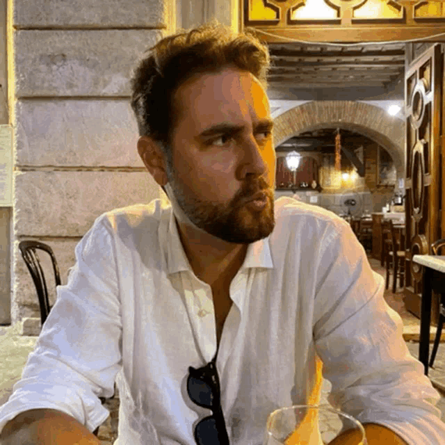 a man with a beard is sitting at a table with a glass in front of him
