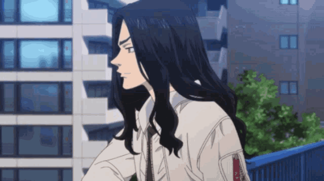 a man with long black hair is standing in front of a building looking out the window .